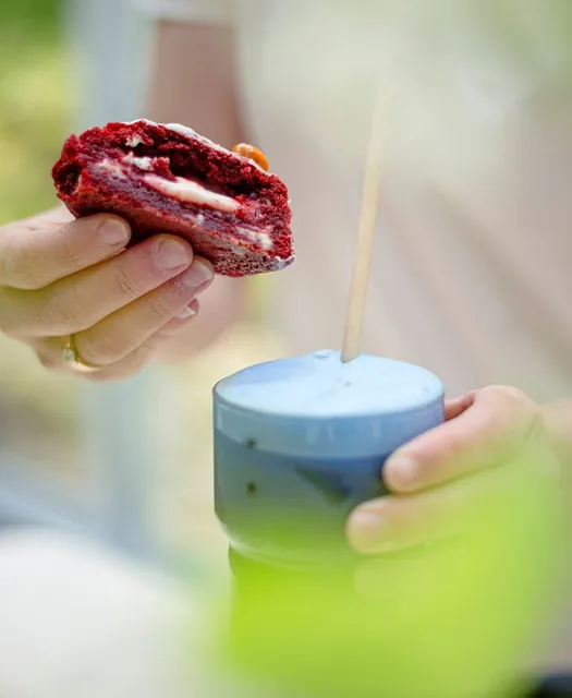 Käsi pitelee halkaistua red velvet -keksiä, vieressä sininen matchajuoma.